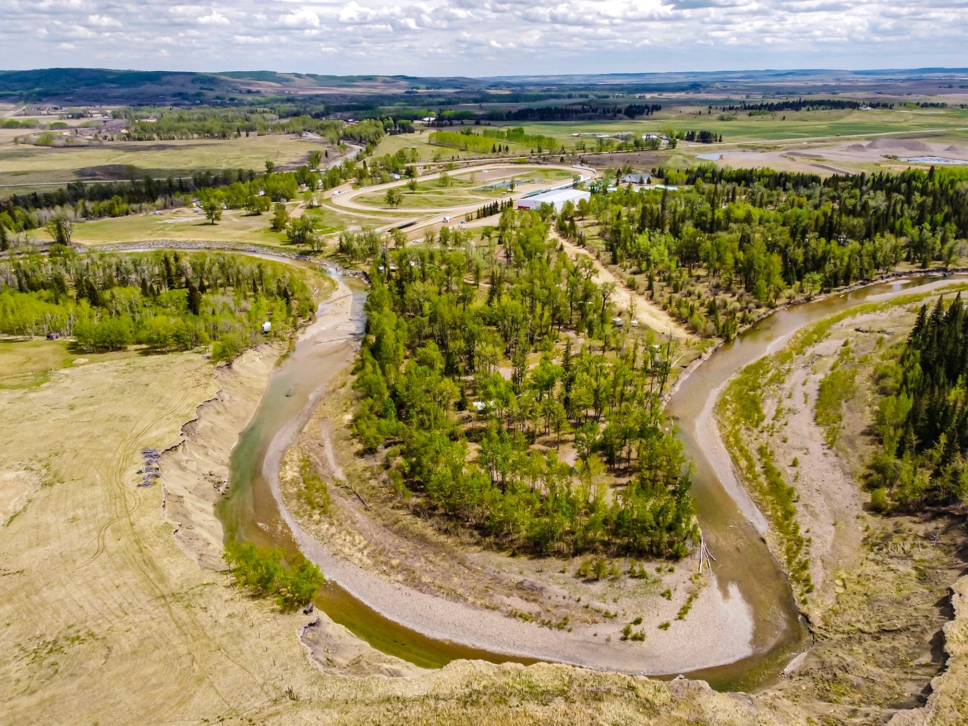 Aerial view of a curved river flowing through trees and open fields at the Millarville Racing & Agricultural Society Campground.