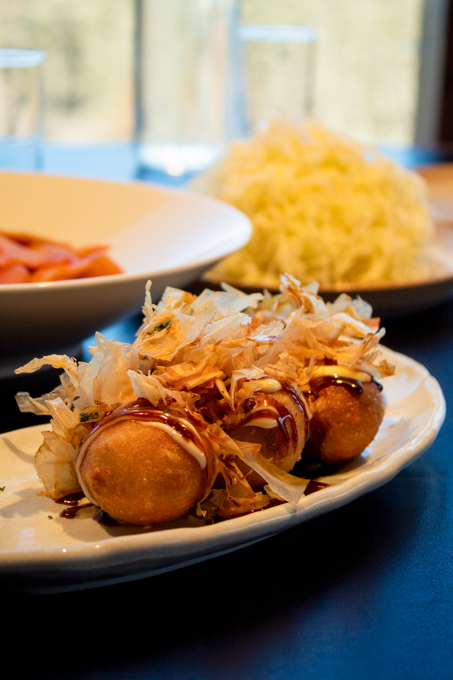 Takoyaki balls topped with sauce and bonito flakes on a plate, salad behind.