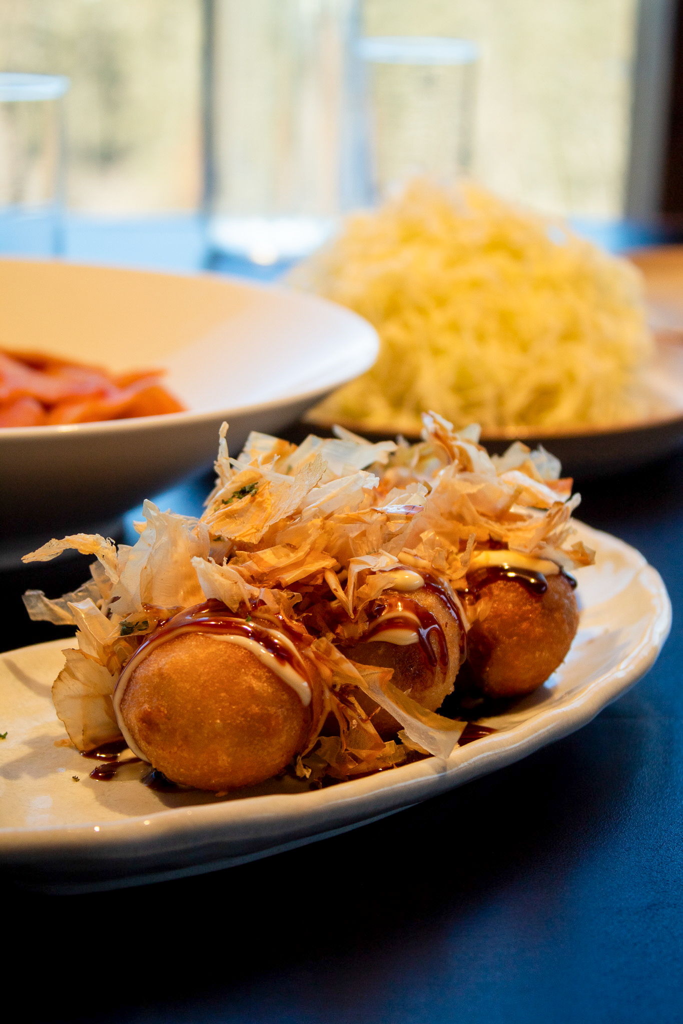 Takoyaki balls topped with sauce and bonito flakes on a plate, salad behind.