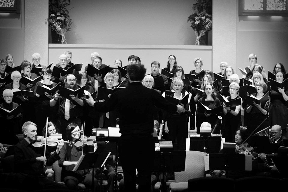 Choir and orchestra performing on stage with conductor leading the ensemble.