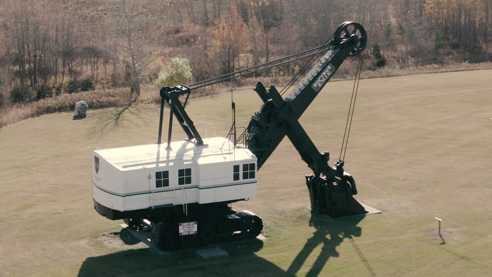 Large vintage Bucyrus excavator displayed on grass field near sparse trees.