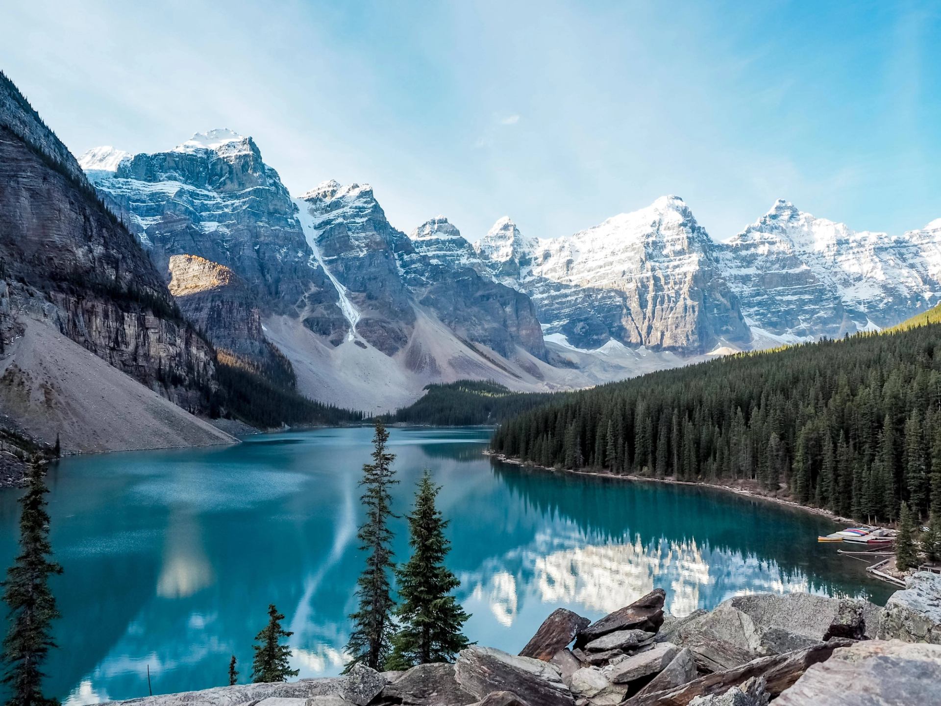 Turquoise mountain lake with snow-capped peaks, dense evergreen forest and rocky shoreline.
