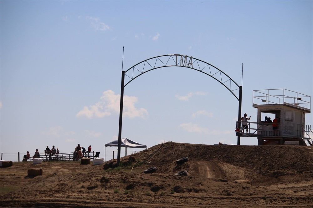 Dirt motocross track with metal arch, spectators on bleachers and elevated booth.