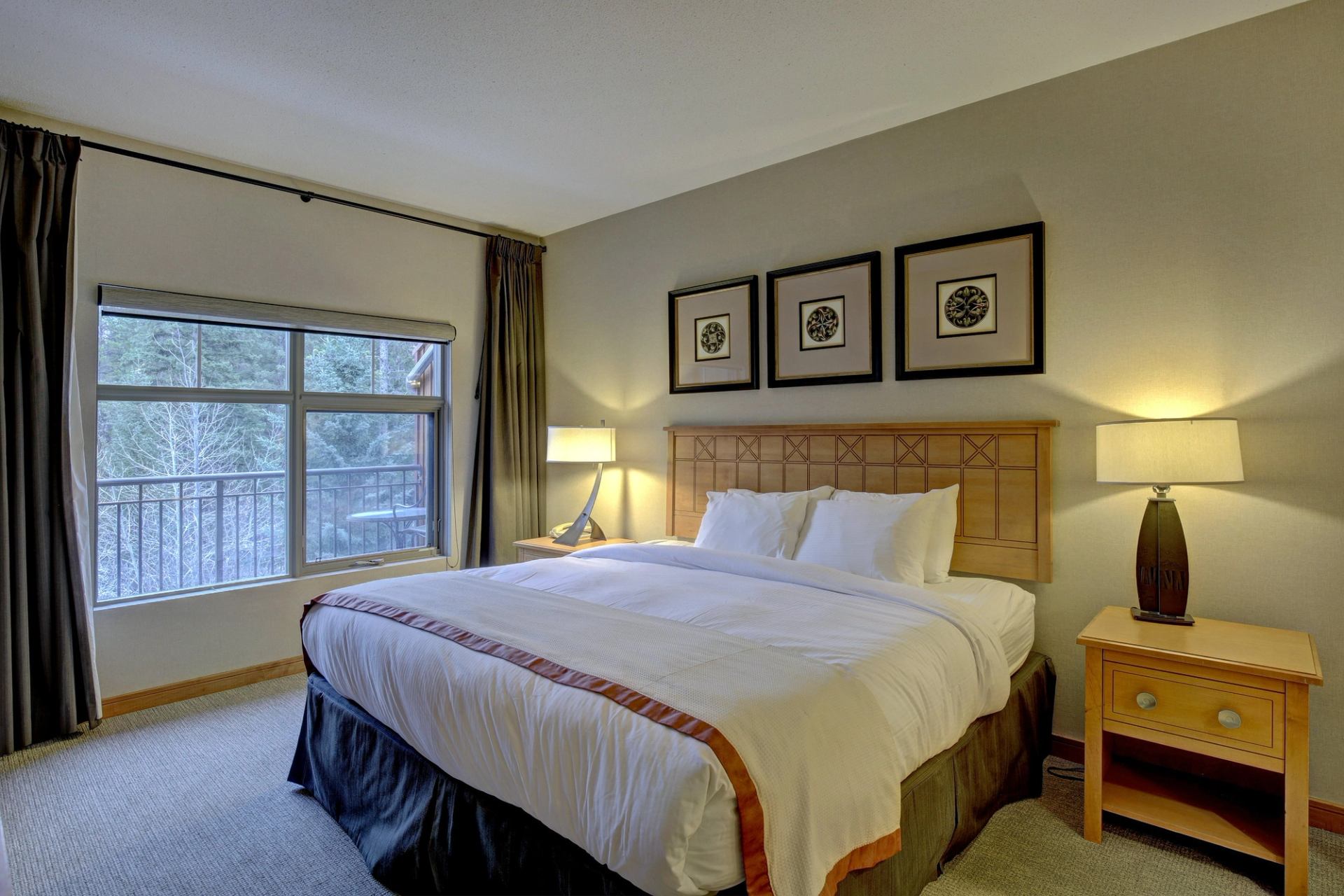 Bedroom with large window, king bed, warm lighting, and nature view outside.