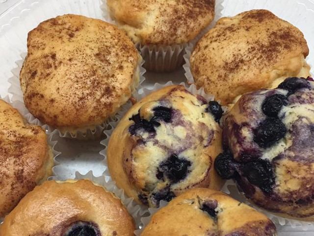 Assorted pastries and muffins with blueberries in paper liners on a tray.