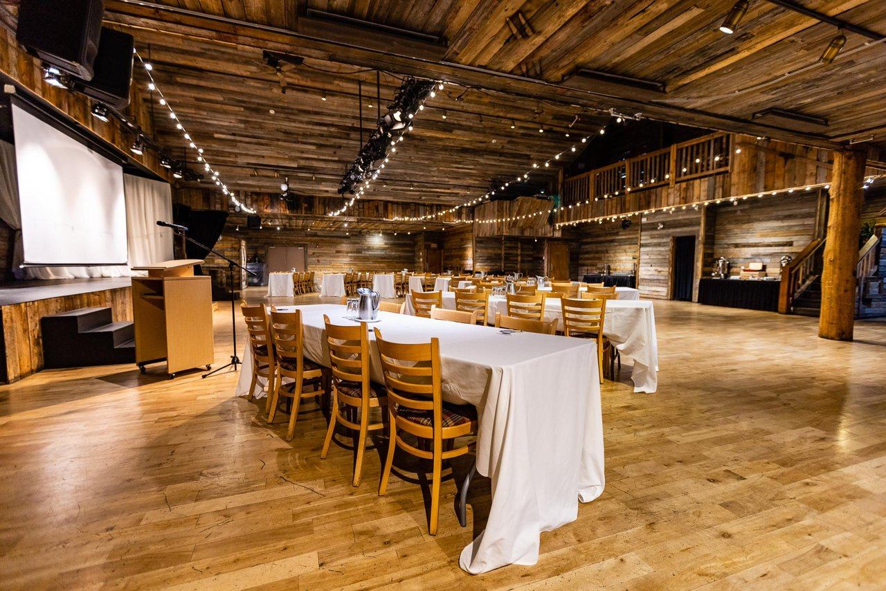Spacious event hall with banquet tables, stage, and overhead string lighting.