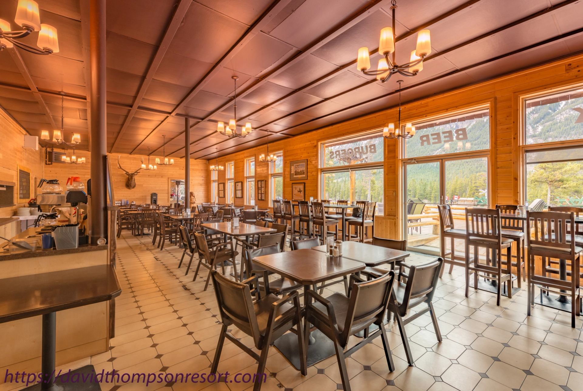 Wood-panelled restaurant dining room with tables, chairs, chandeliers and large windows.