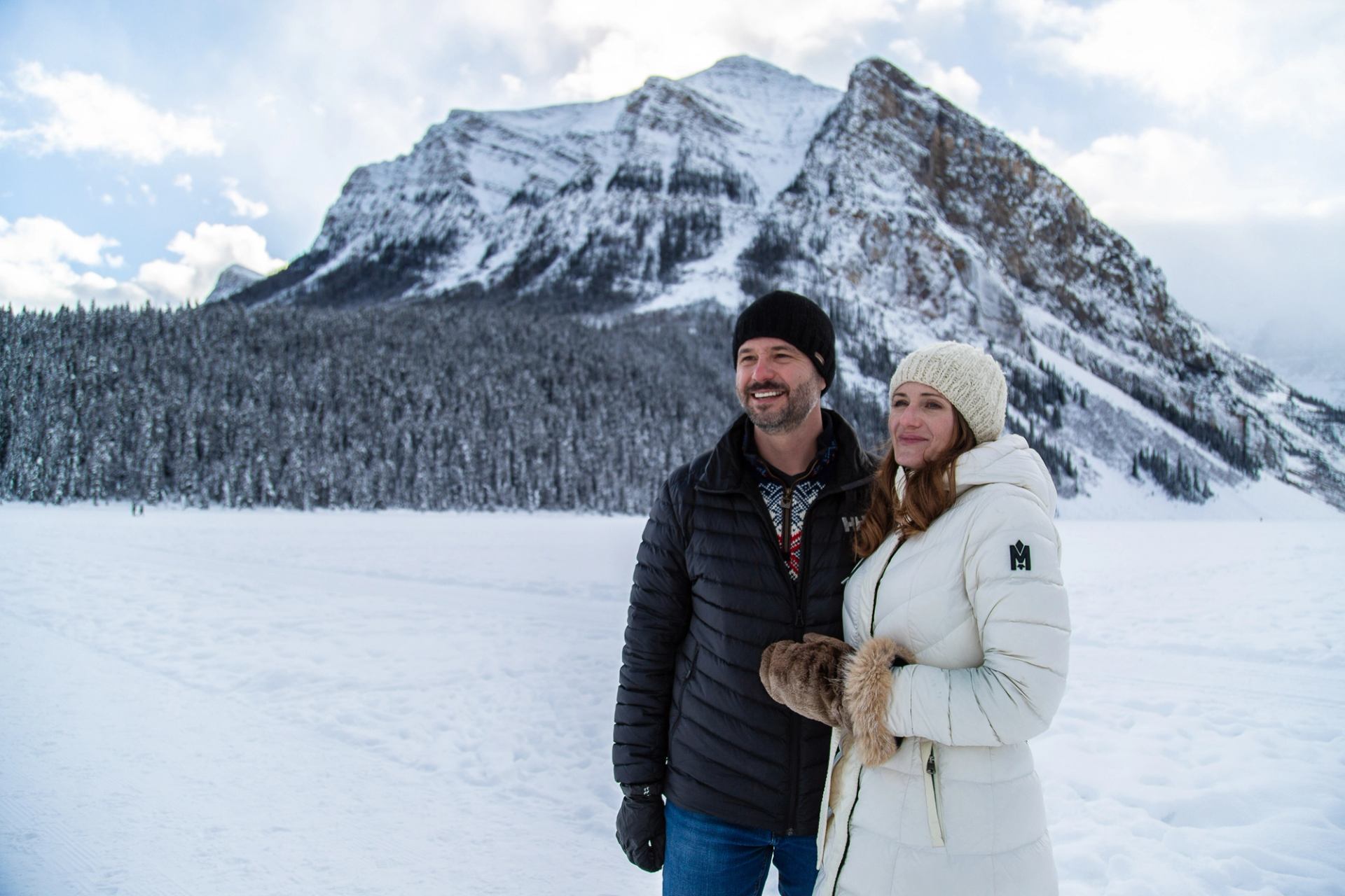 Two people standing on a snowy frozen lake with towering mountains in the background.
