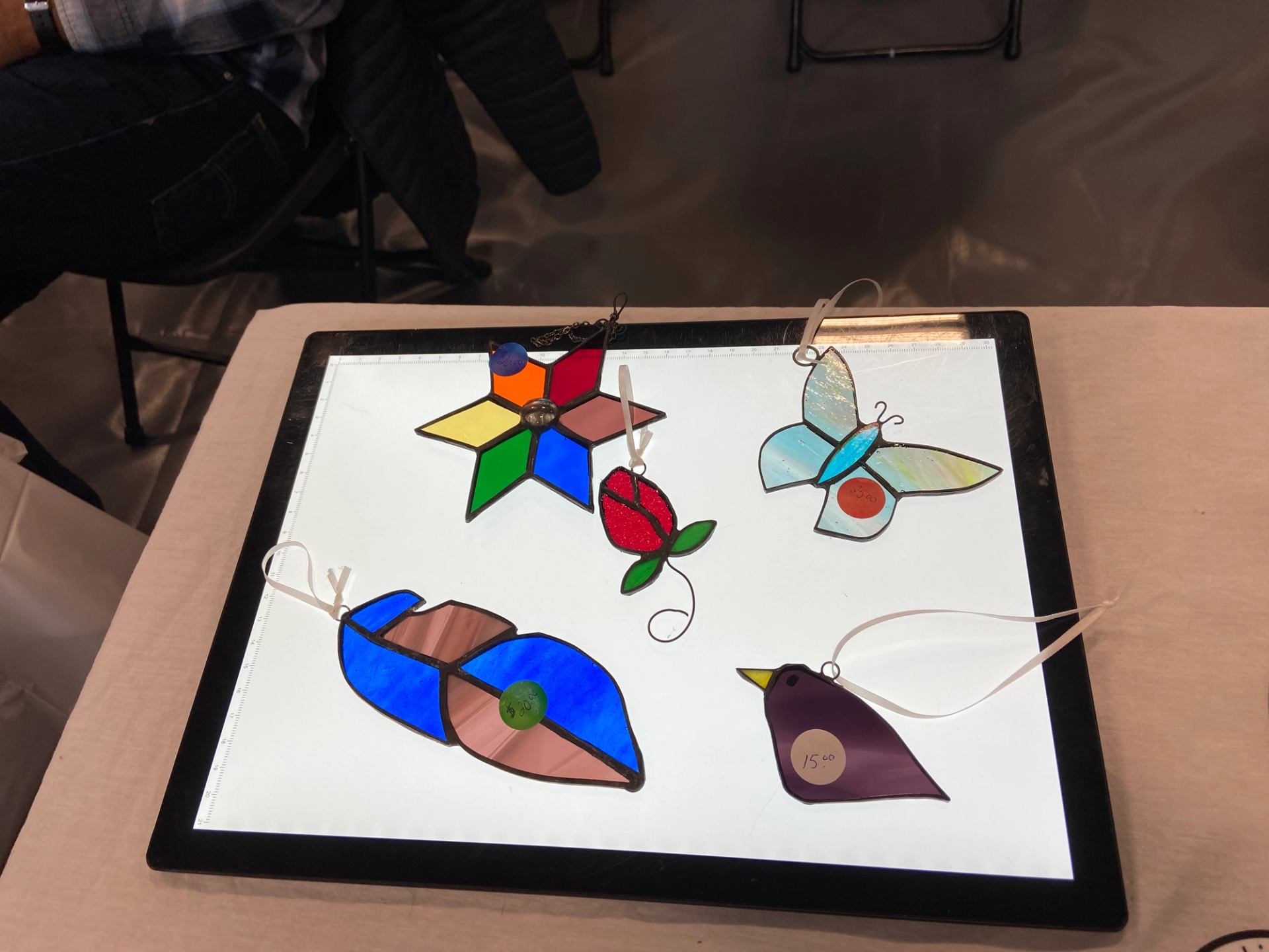 Colorful stained glass ornaments displayed on a lighted panel.