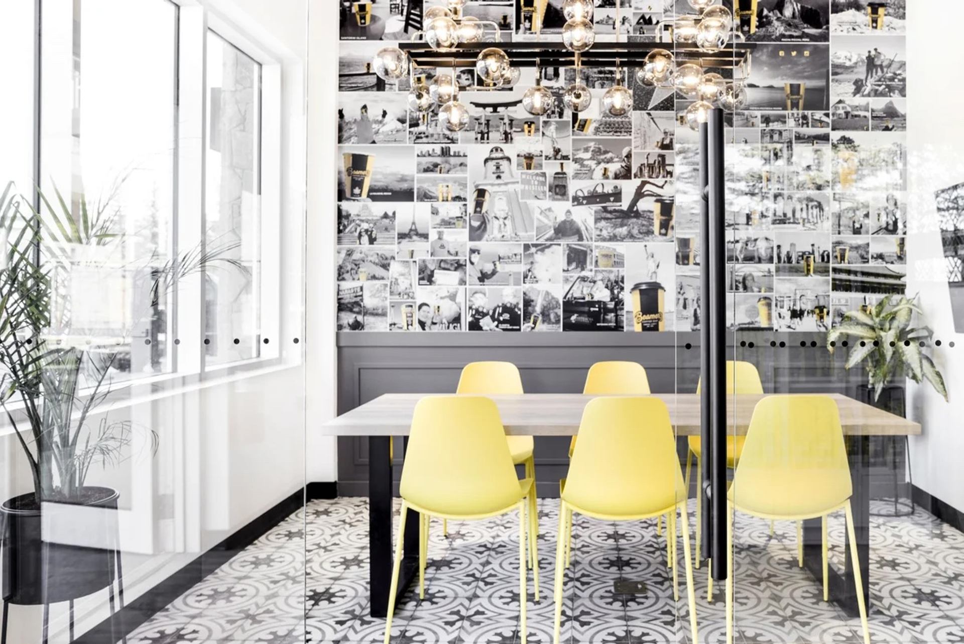 Modern meeting room with yellow chairs, photo‑collage wall, and bright natural light at Beamer’s Coffee.