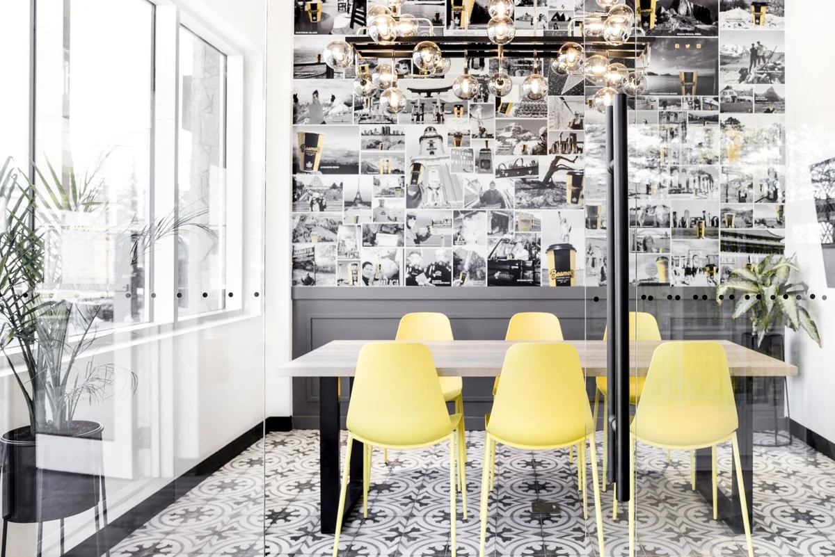 Modern meeting room with yellow chairs, photo‑collage wall, and bright natural light at Beamer’s Coffee.