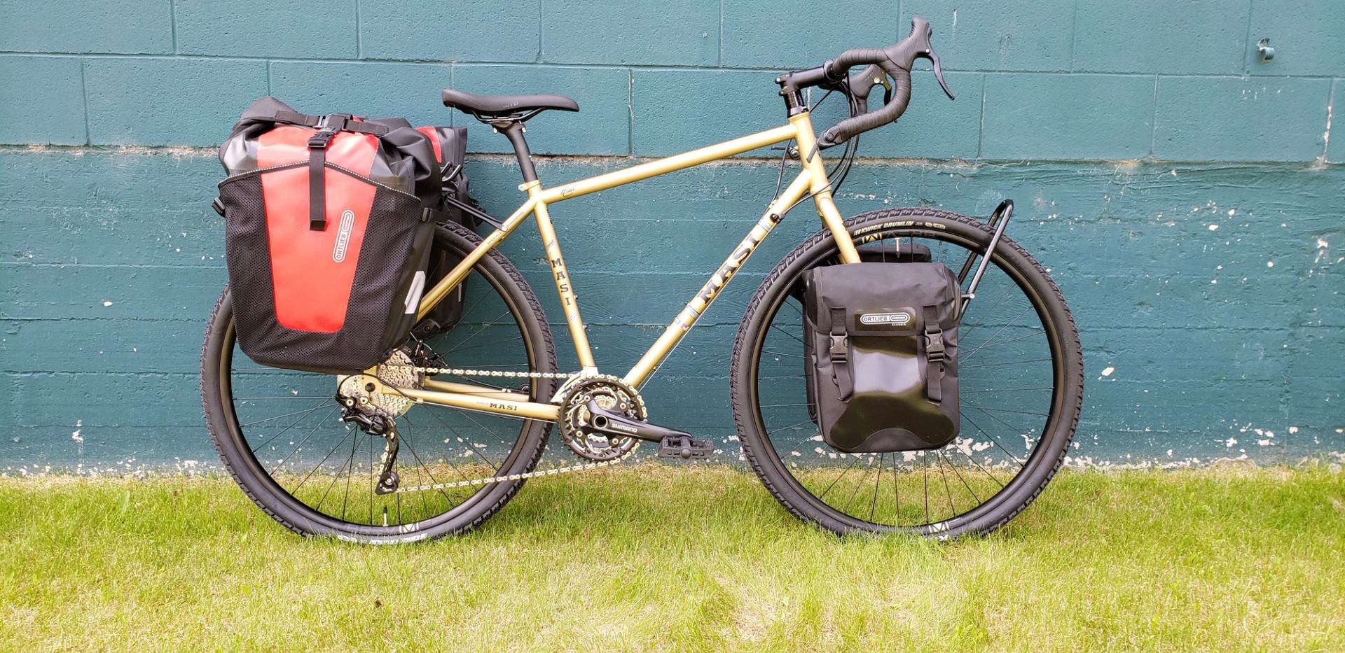 Yellow bike with red and black panniers by a teal wall.