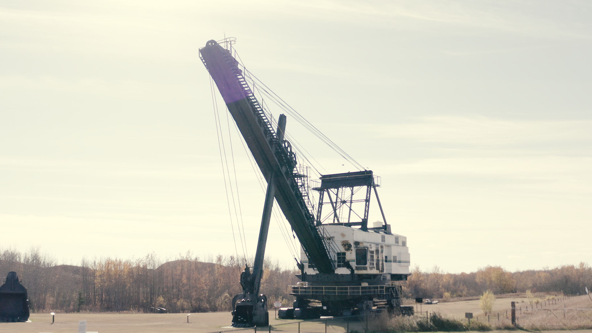 Large dragline excavator with raised boom stands on open ground near distant trees.