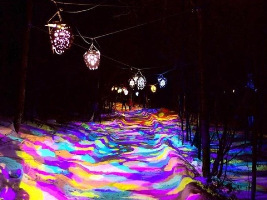 Snowy path lit by colorful lanterns and glowing lights at night.
