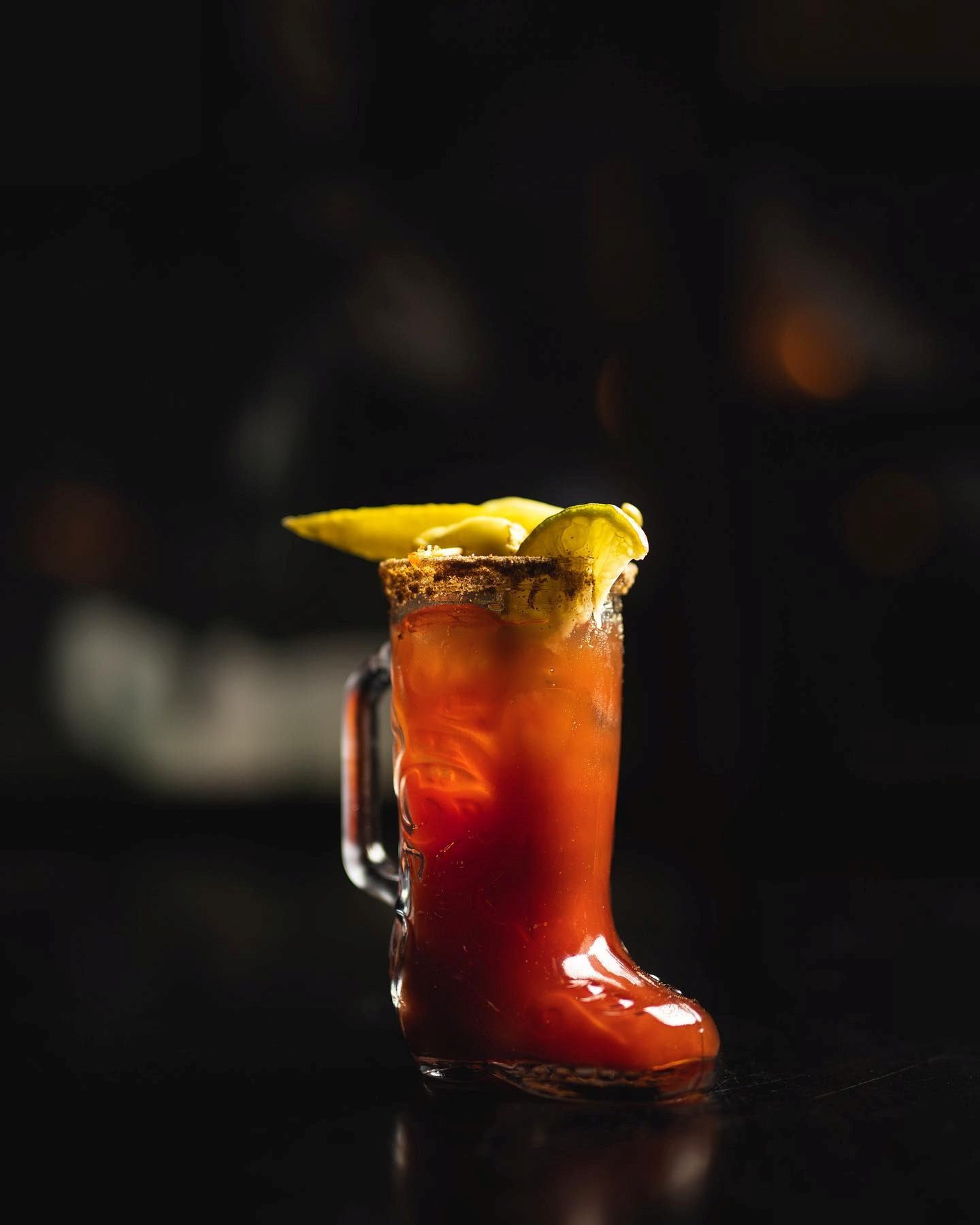 Boot-shaped glass with red cocktail and citrus garnish.