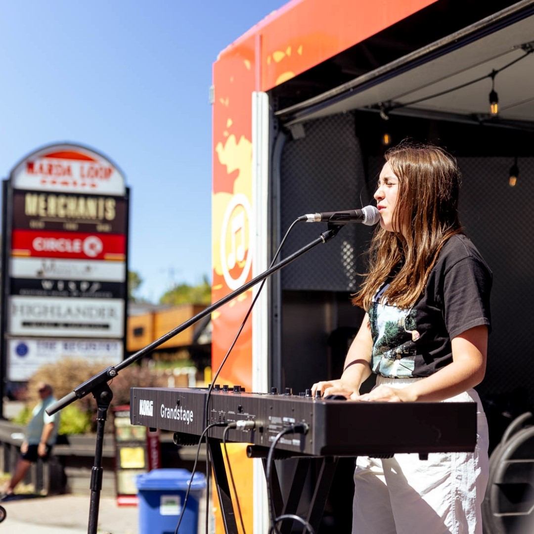 Female musician sings at outdoor stage with microphone and keyboard at street festival in Calgary.