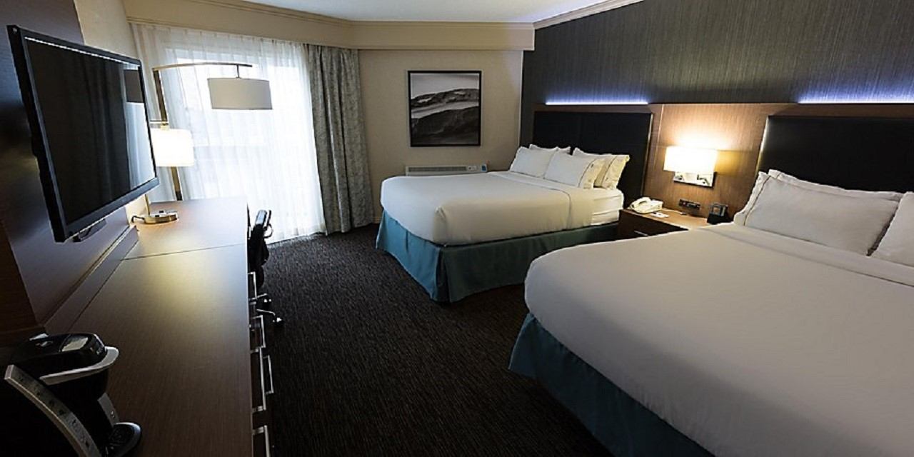 Modern guest room with two beds, desk, and large TV.