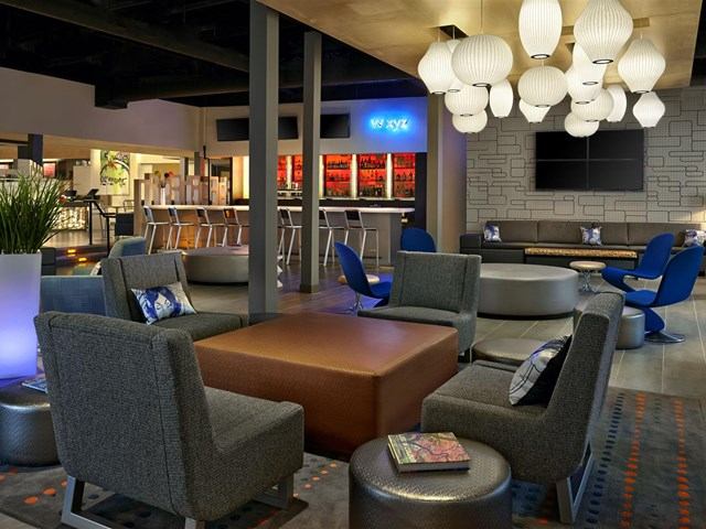 Stylish lounge with modern seating, neon bar sign, and TVs at Aloft Calgary University.