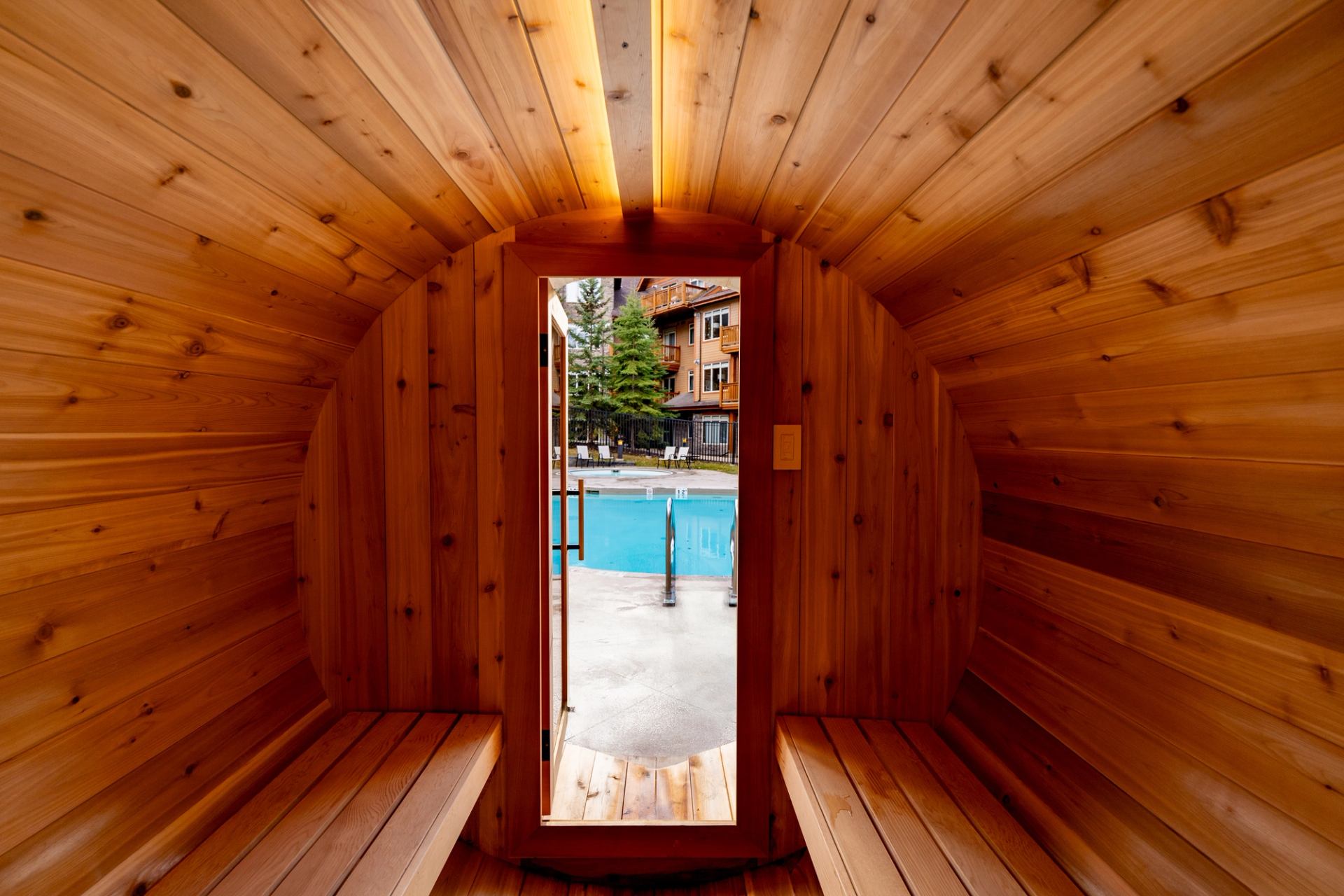 Wood-panelled sauna with benches and an open doorway overlooking an outdoor pool.