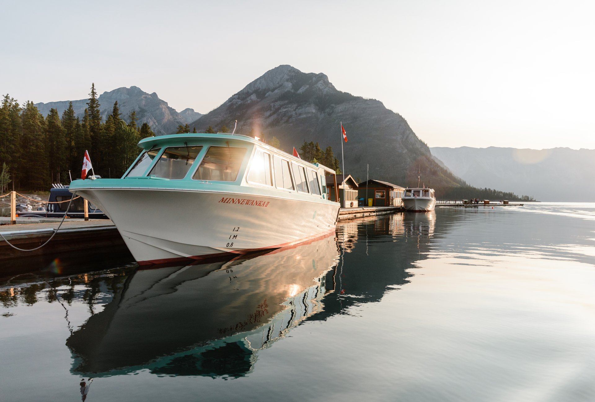 Tour boat docked on a calm lake with tall mountains in the background at sunset.