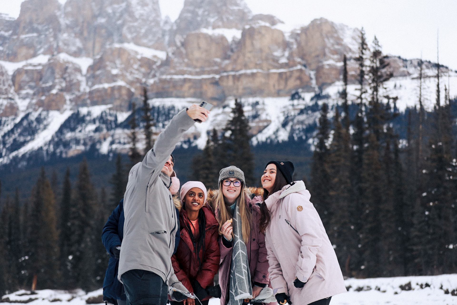 Group taking a selfie in snowy Banff with towering rocky mountains in the background.