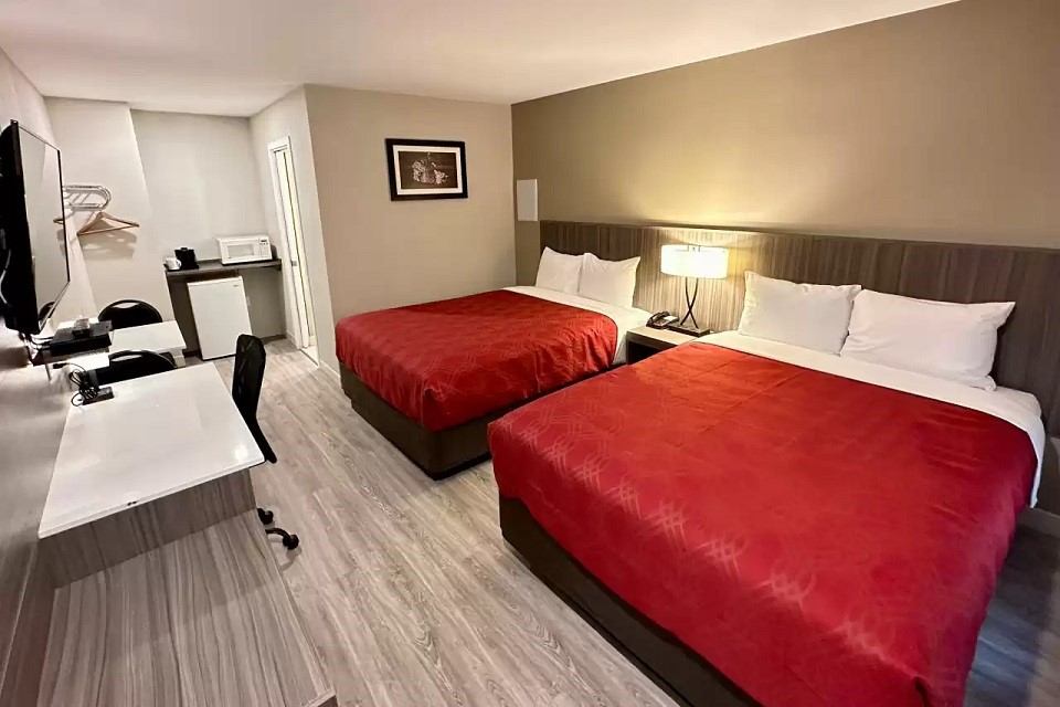 Hotel room with two red-covered beds, desk, TV, and kitchenette area.