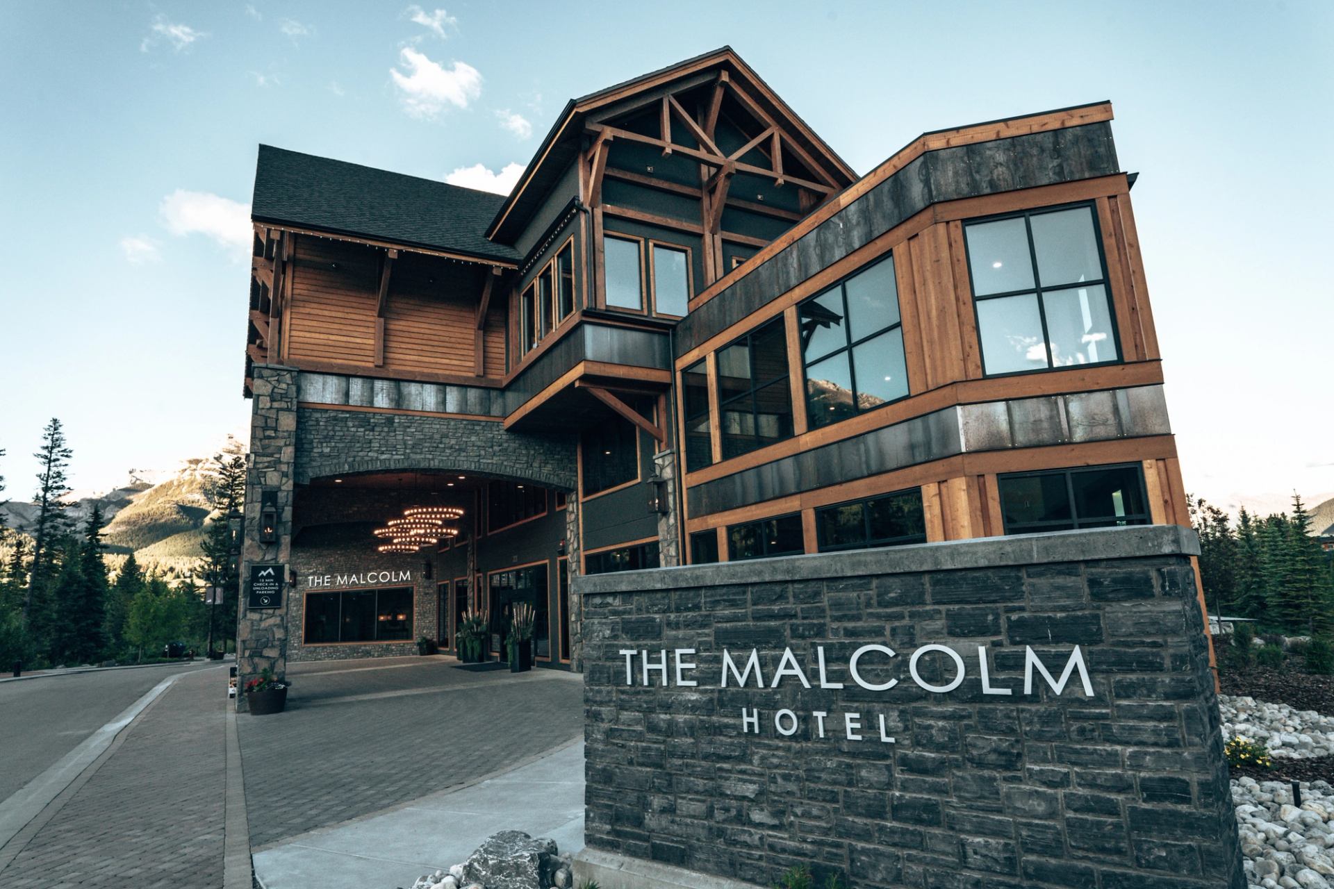 A modern lodge-style hotel exterior with stone and wood details against a mountain backdrop.
