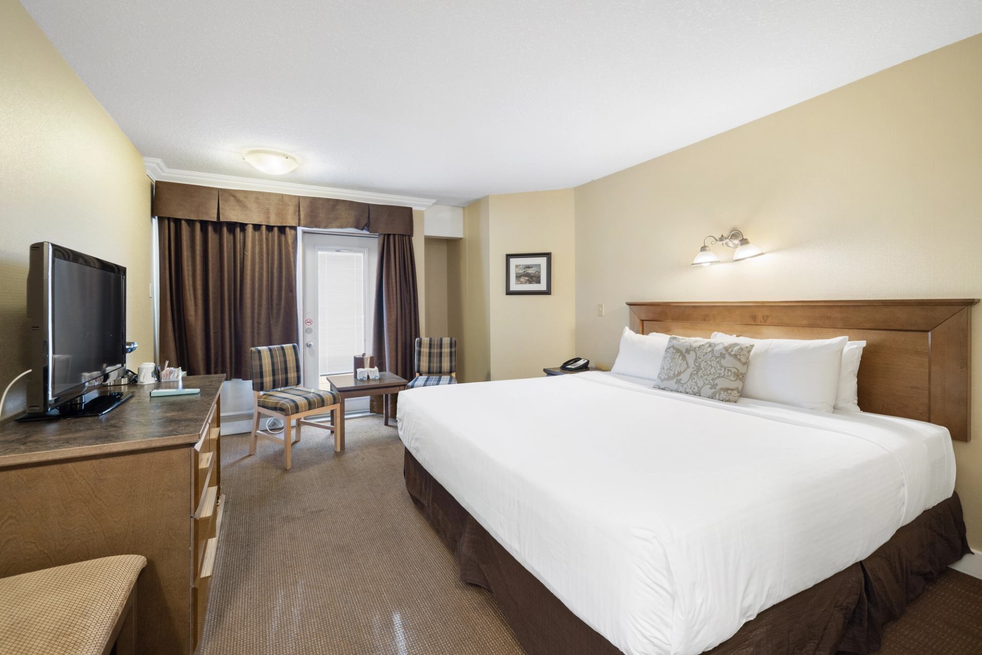 Neat hotel room with large bed, armchair, TV and soft lighting.