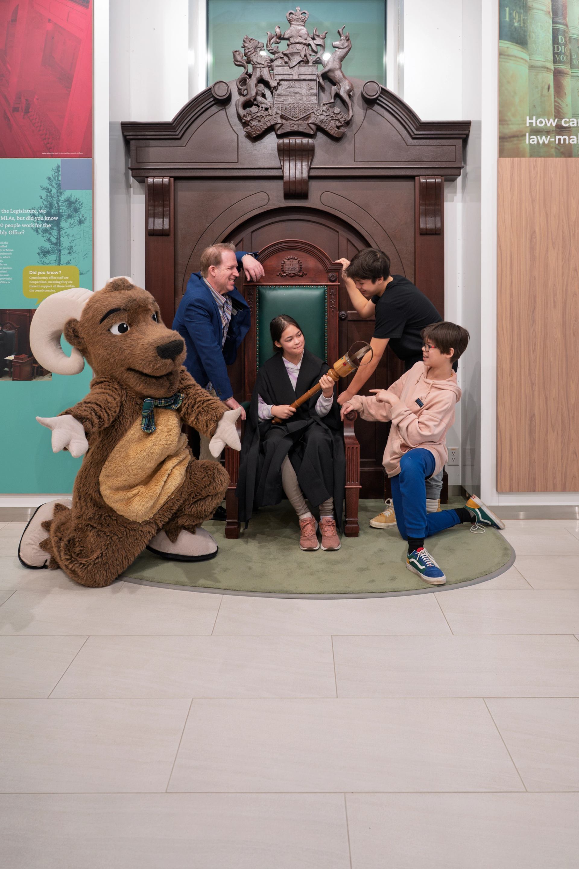 Group with horned mascot posing by ornate chair in ceremonial setting.
