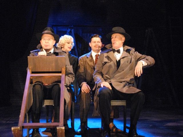 Dramatic scene with four performers under blue lights.