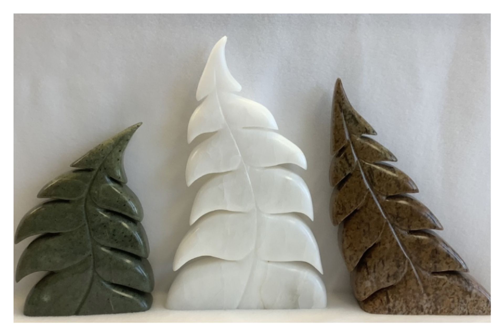Three carved stone leaf sculptures in green, white and brown on a plain background.