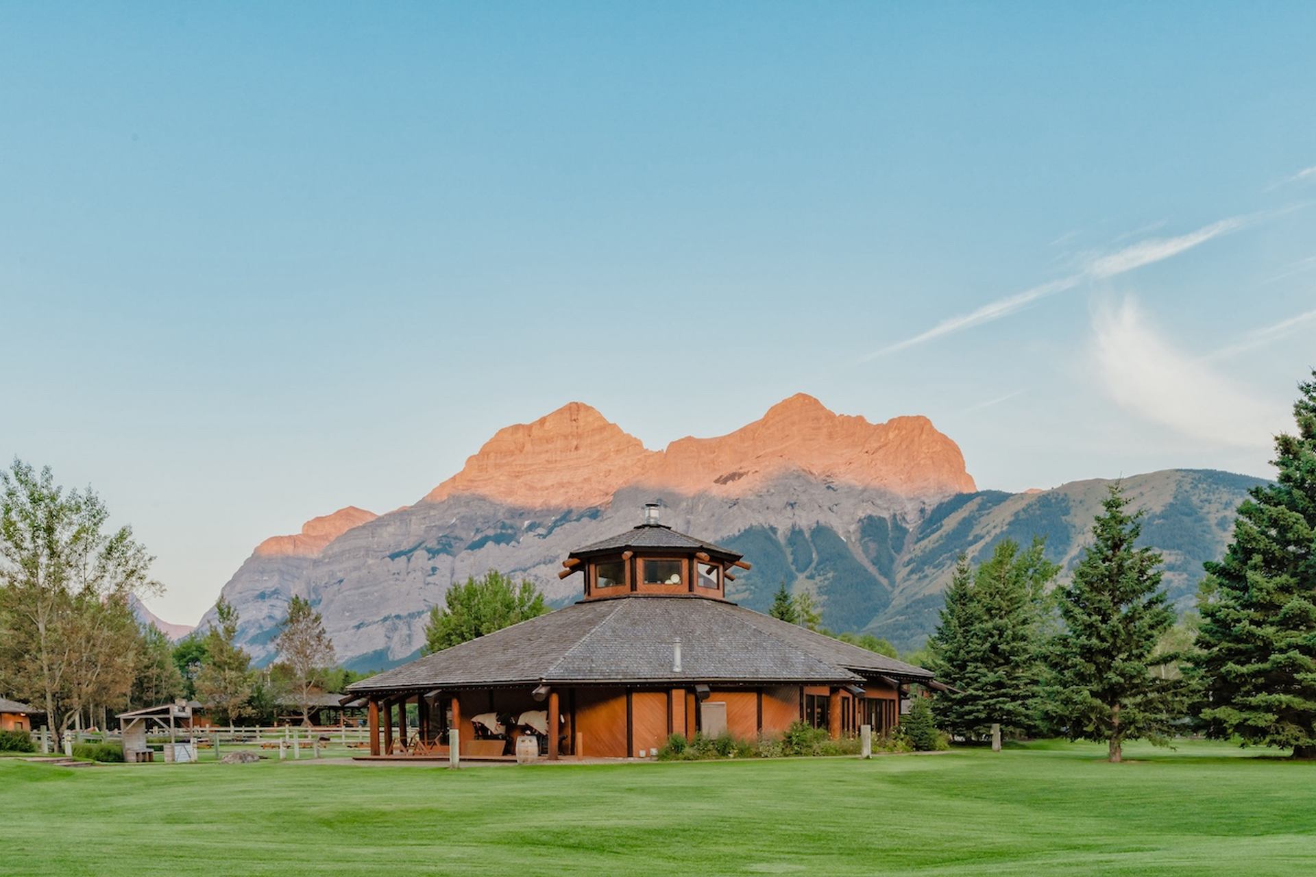 Wooden ranch building with wide lawns and tall mountain peaks in the distance.