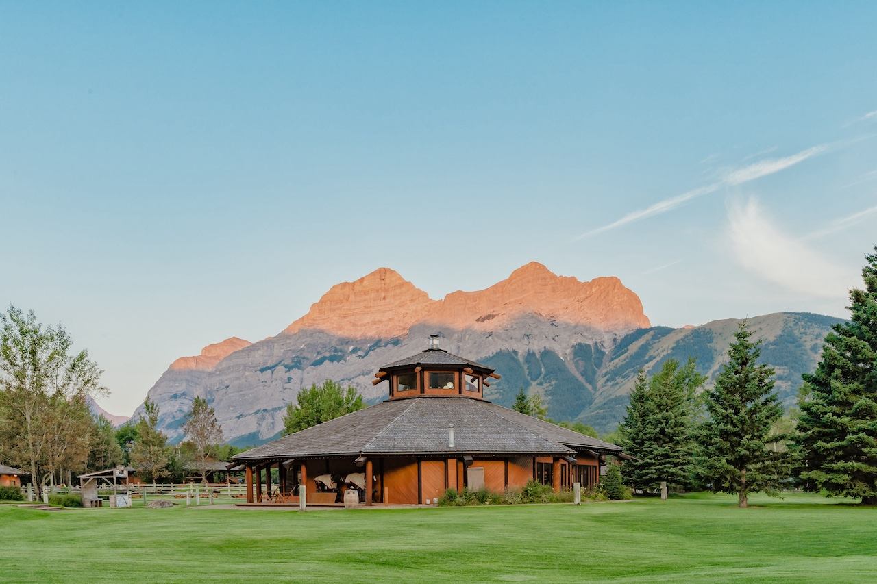 Wooden ranch building with wide lawns and tall mountain peaks in the distance.