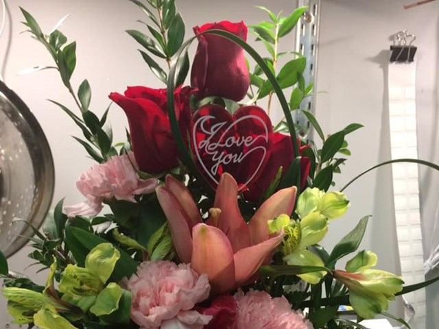 Flower arrangement with red roses, pink lilies, carnations and heart decoration reading I love you.