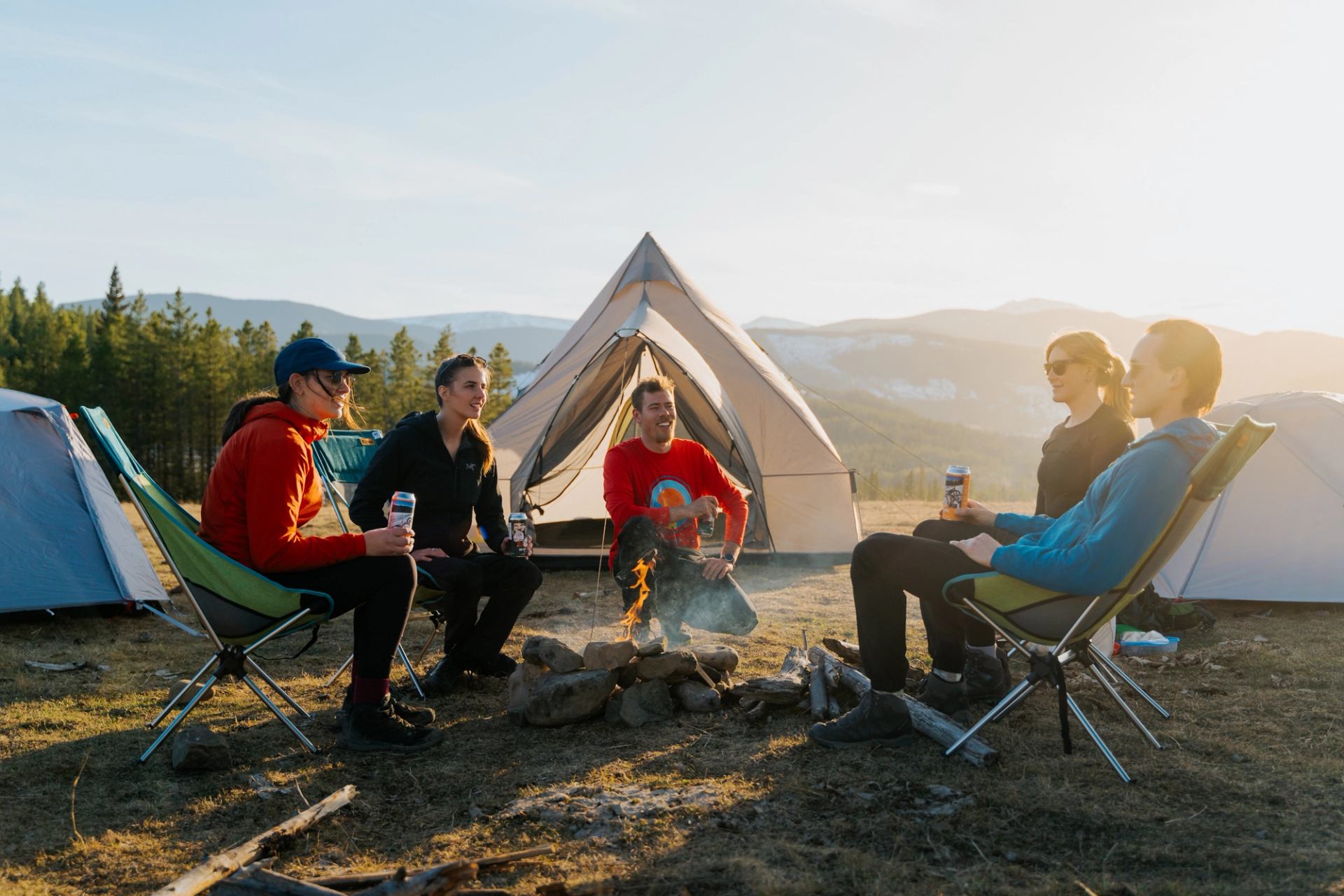 Campsite with four people seated by a fire and a large tent in a forested valley.