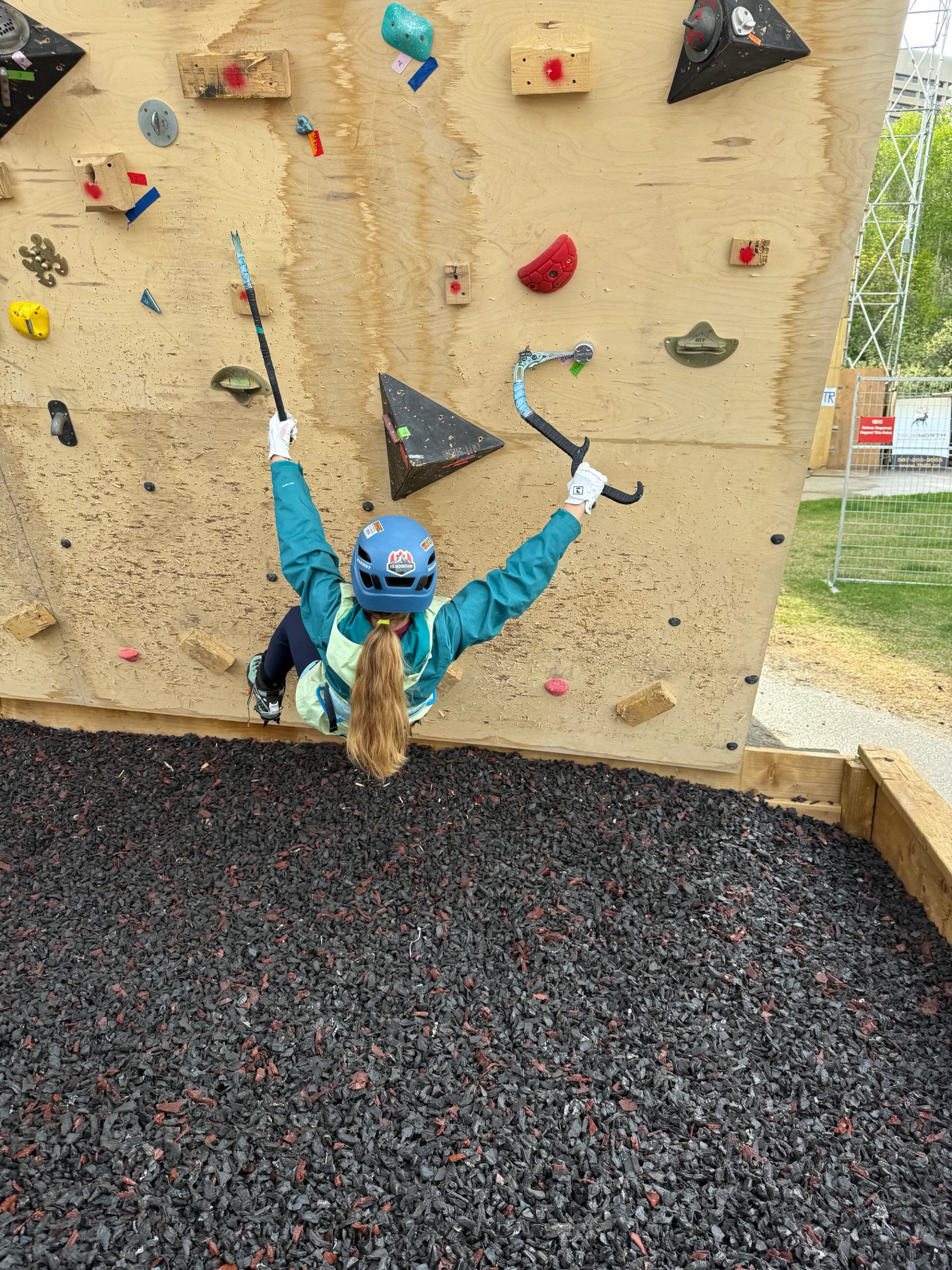 Climber practicing dry-tooling on a wooden wall with ice axes at Climb YEG.