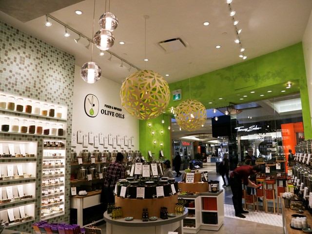 Olive oil shop interior with green walls, product displays, and shoppers.
