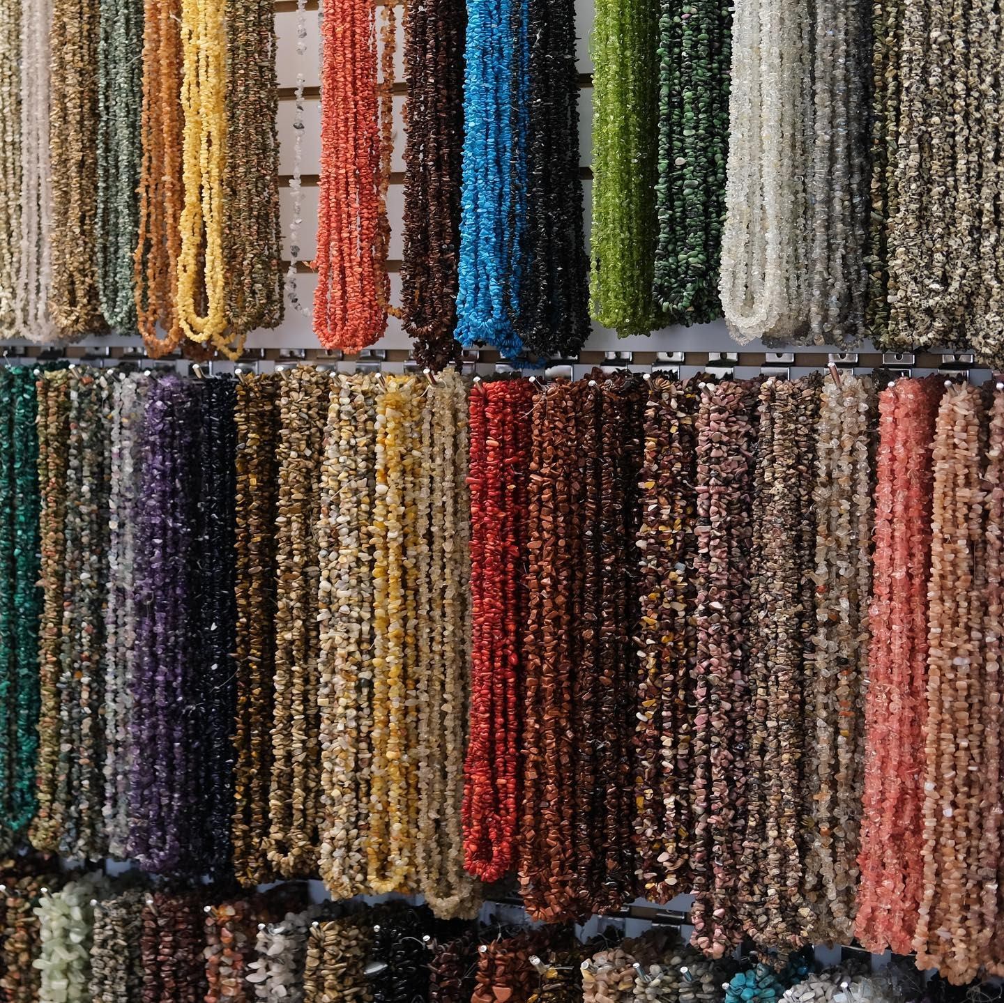 Rows of colourful stone chip bead strands hanging on slatwall display.