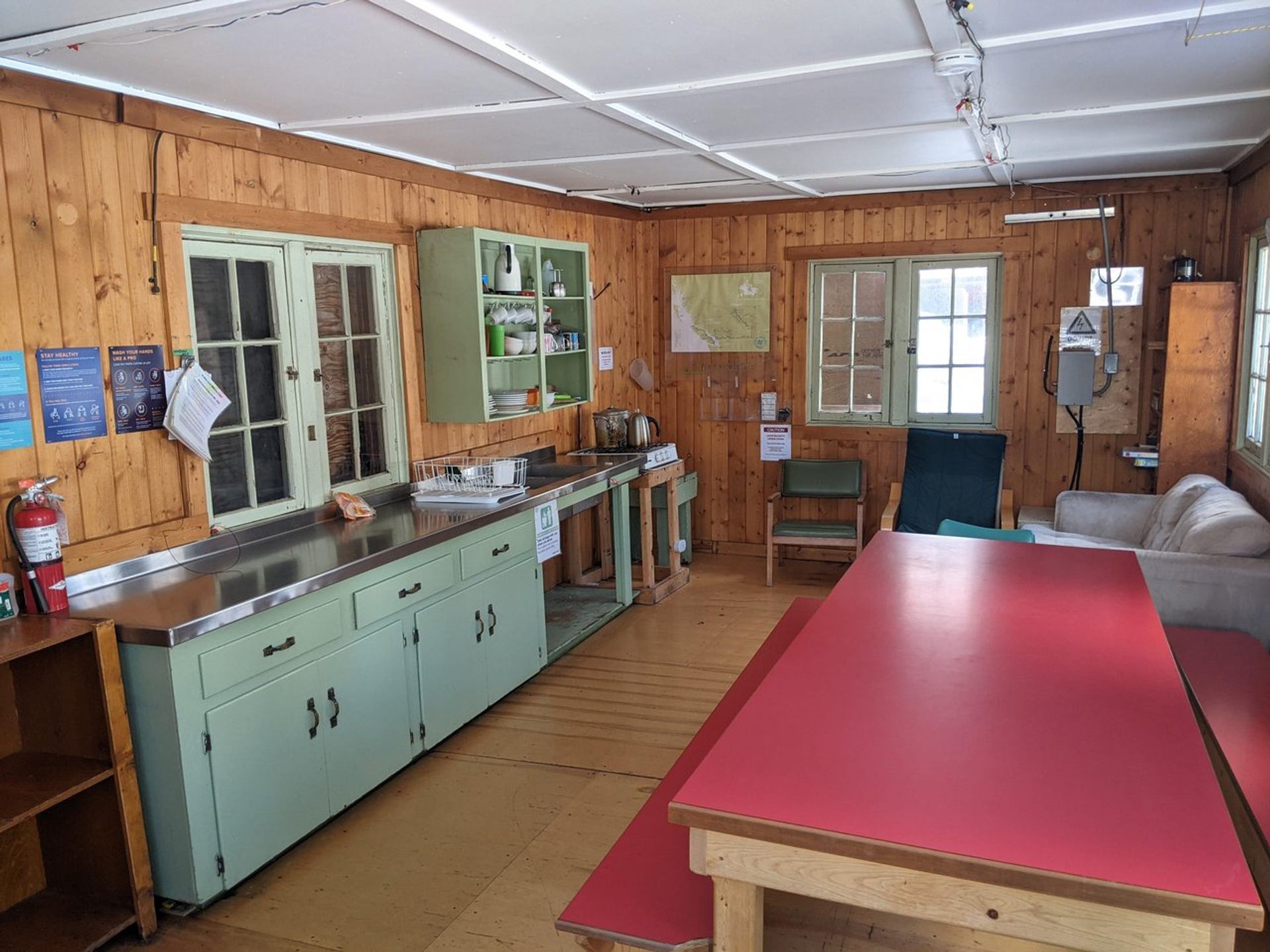 Kitchen and dining area with rustic green cabinets, wooden walls, large red dining table.