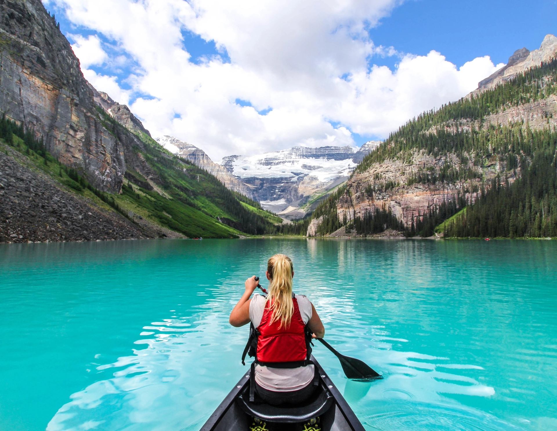 A person canoes on a vibrant turquoise lake surrounded by mountains and glaciers.