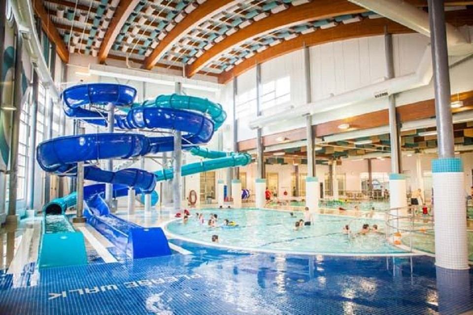 Indoor pool with large blue slide, swimmers, and colorful ceiling panels.