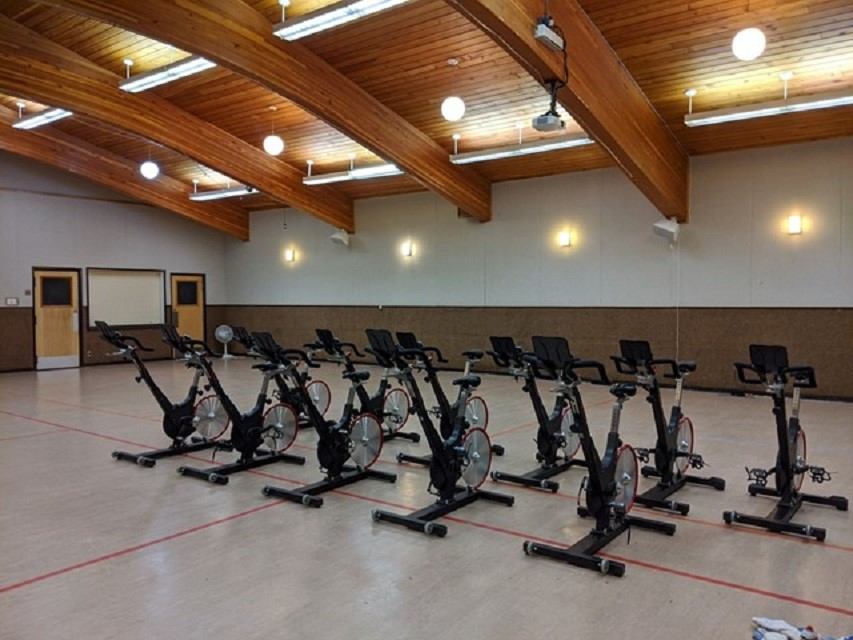 Row of stationary exercise bikes inside Beaverlodge Recreation Centre gym with wooden ceiling and li.