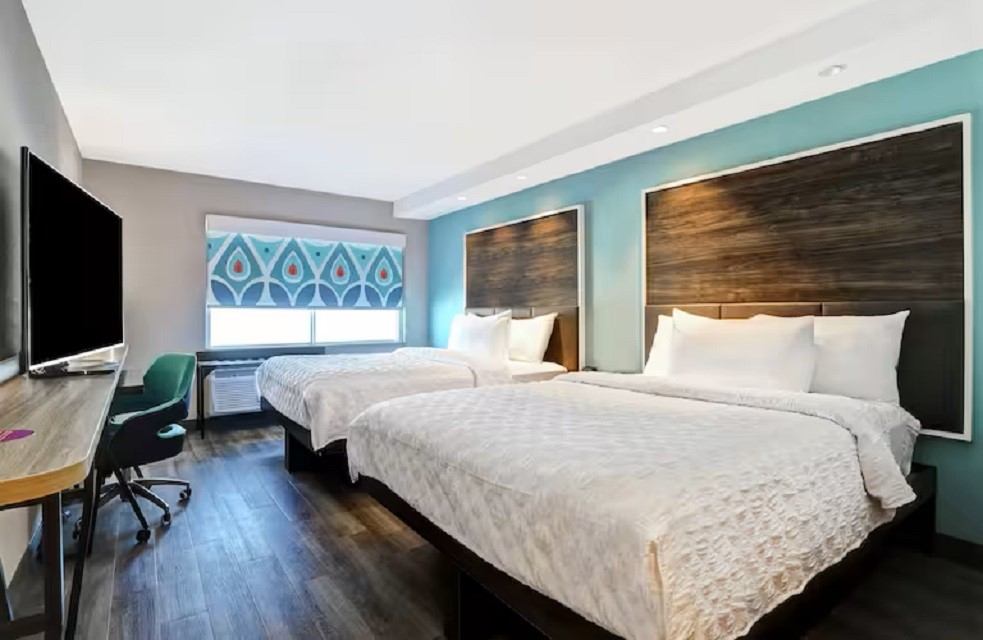 Guest room with two queen beds, teal accent wall, and large flat-screen TV