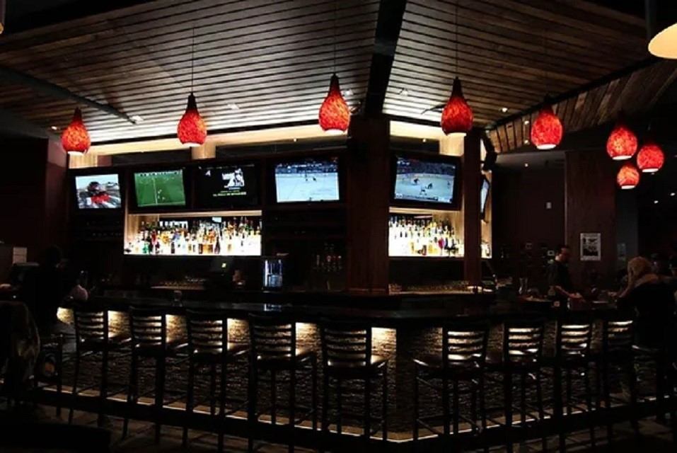 Modern sports bar with multiple TVs, red pendant lights, and a long seating counter