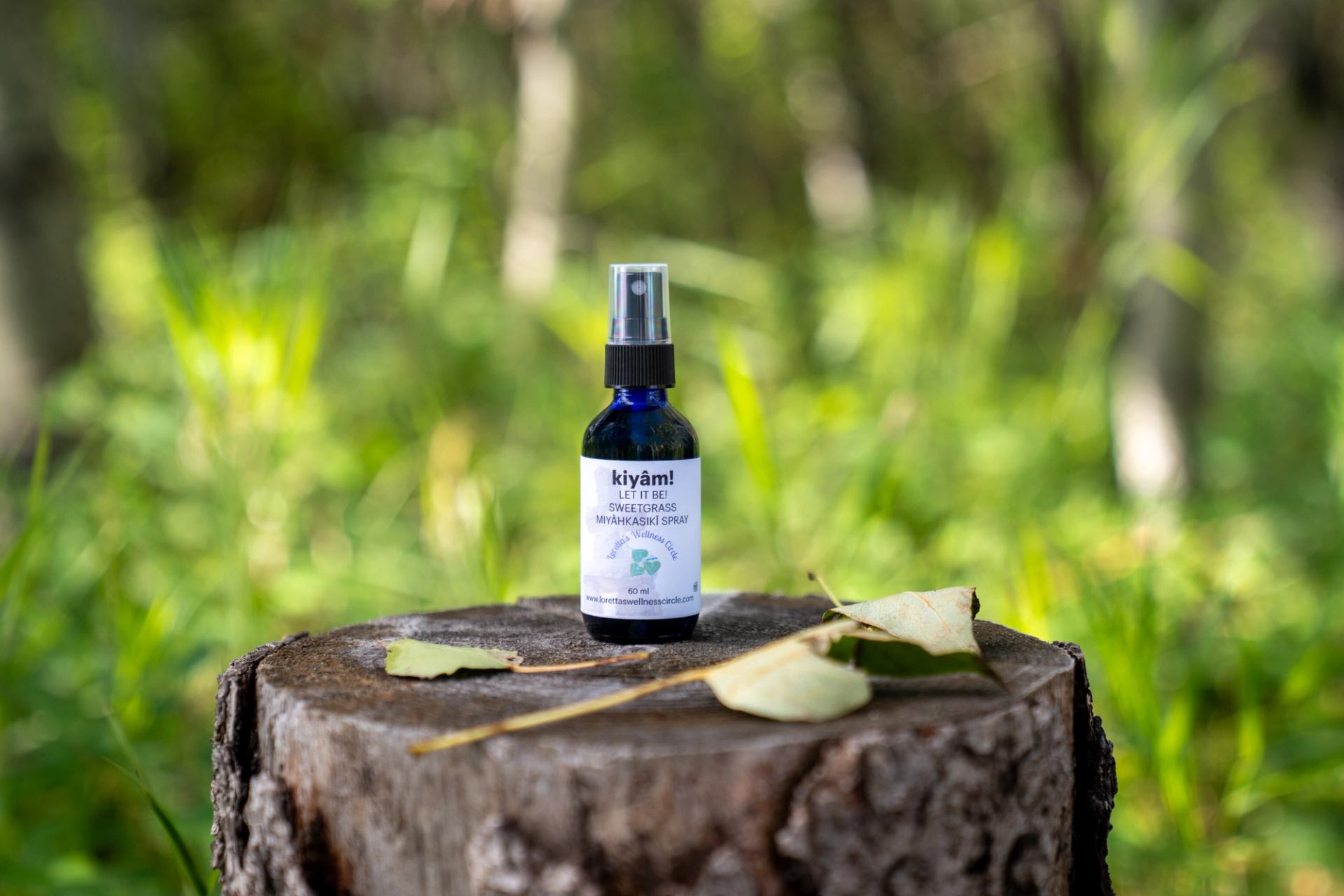  A small wellness spray bottle sits on a tree stump with leaves nearby.
