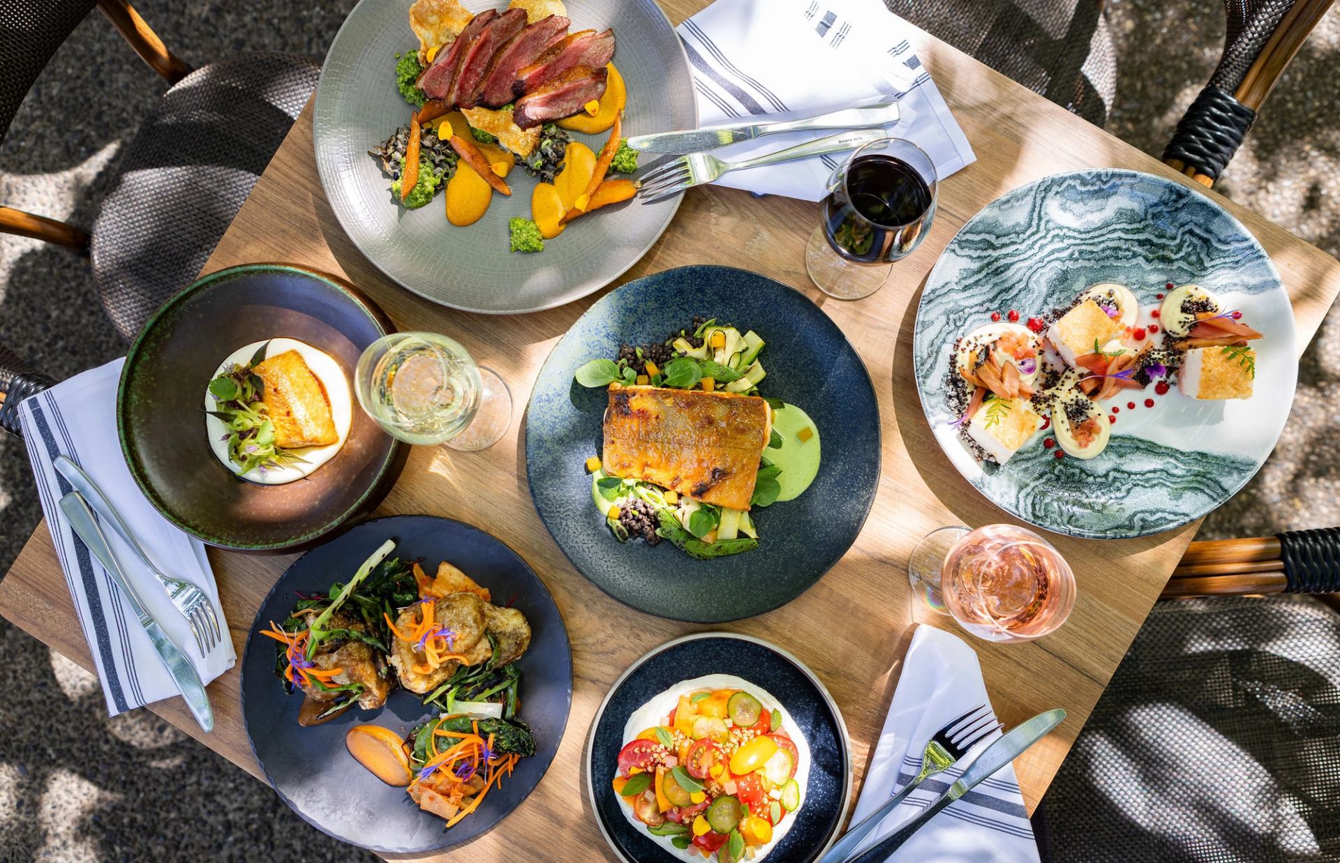 Restaurant table displays colourful plated dishes with glasses of wine and cutlery.
