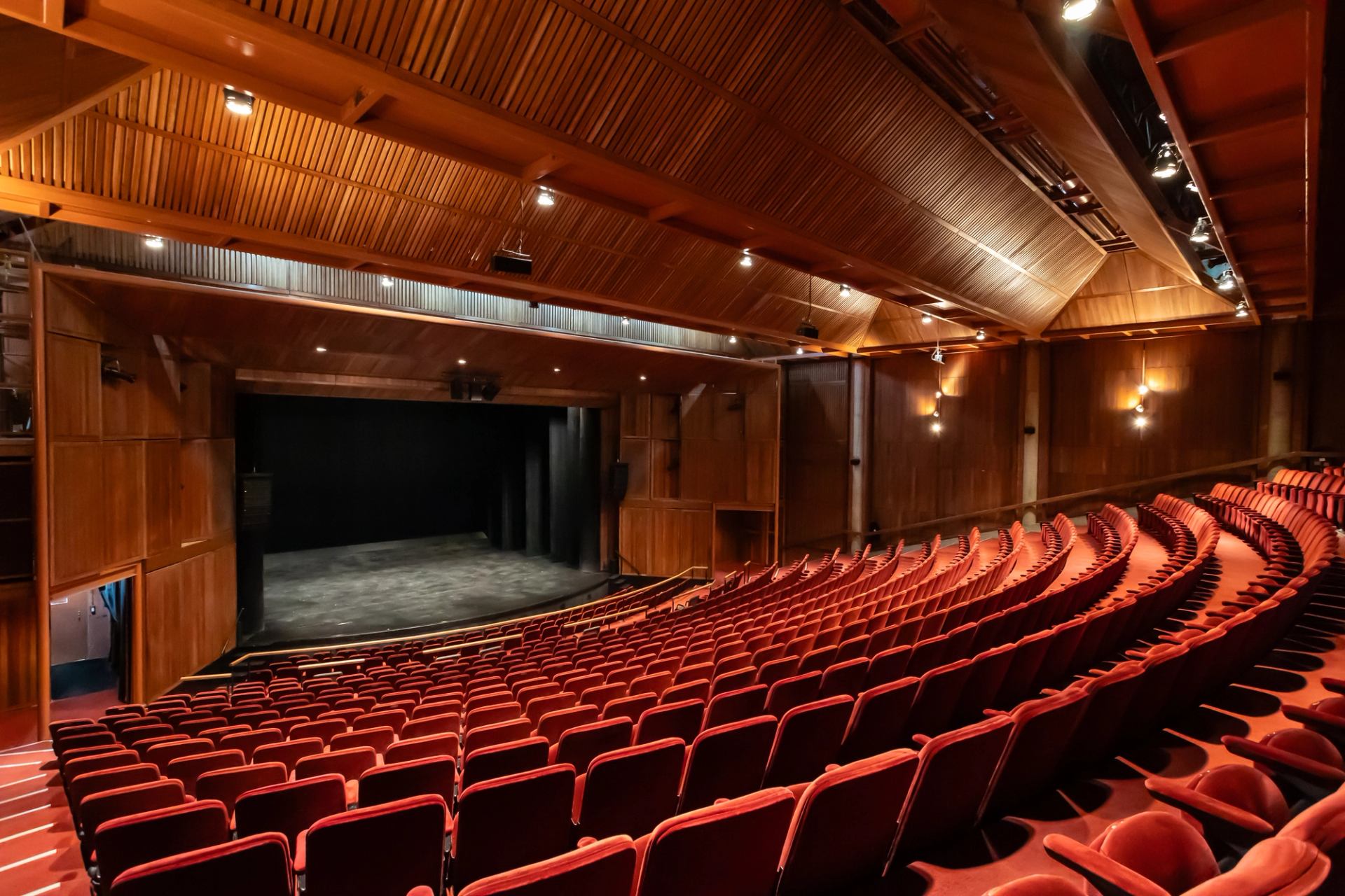 Empty theatre auditorium with curved rows of red seats facing a dark stage.
