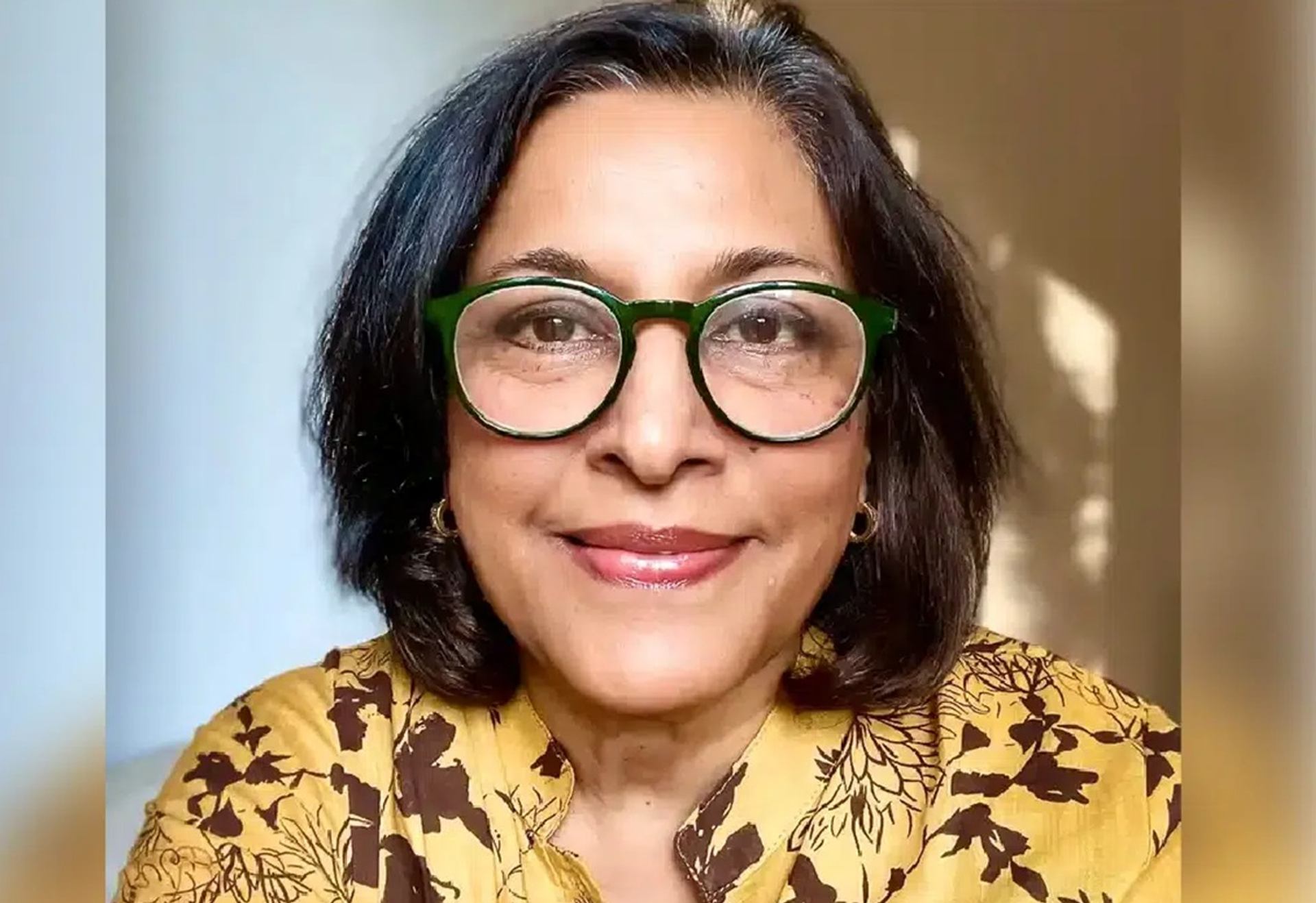 Person wearing green glasses and a yellow floral top faces the camera.