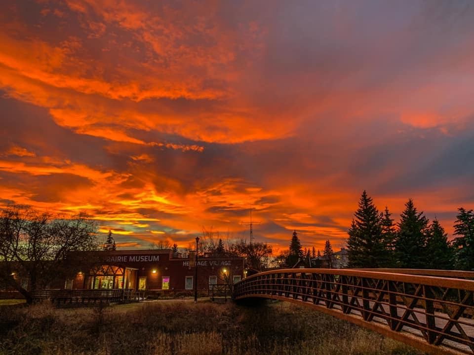 Sunset over bridge and museum building with glowing windows and trees.