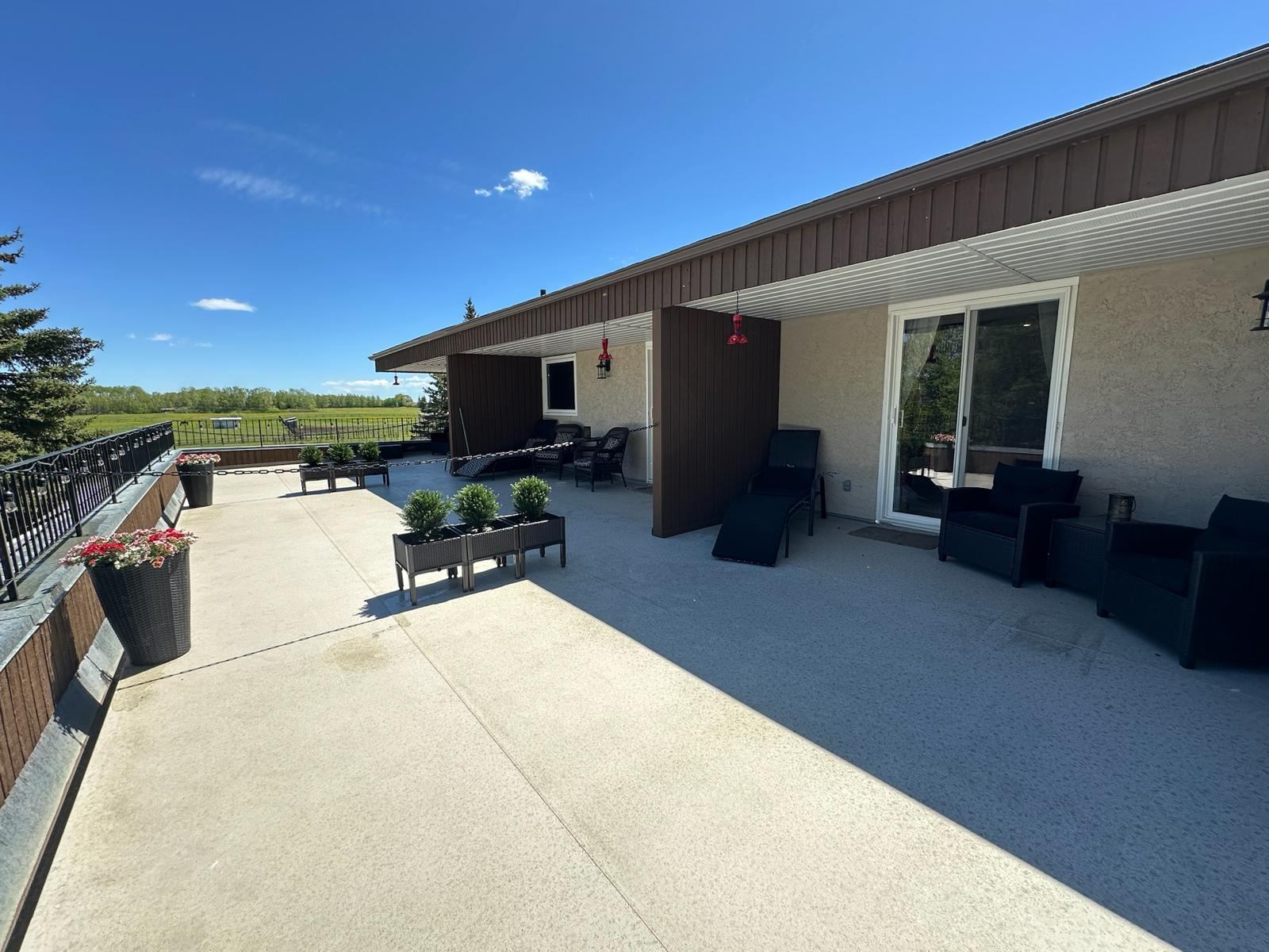 Spacious rooftop patio with lounge chairs, potted plants and railing overlooking green fields.